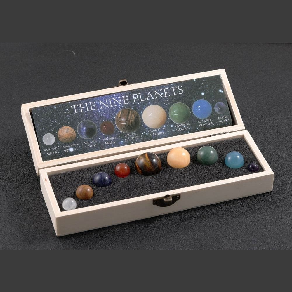 Geoeffnete cremefarbene Holzbox mit neun Natursteinkugeln in Schaumstoffmulden, im Deckel eine Karte mit den Planetennamen